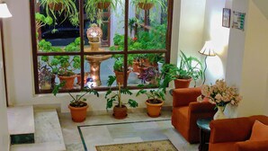 Una habitación con un ventanal grande, una fuente, plantas en macetas, una alfombra estampada y muebles color naranja.