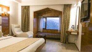 Una habitación de hotel con una cama grande, una silla, una mesita, un banco y un televisor montado en la pared.