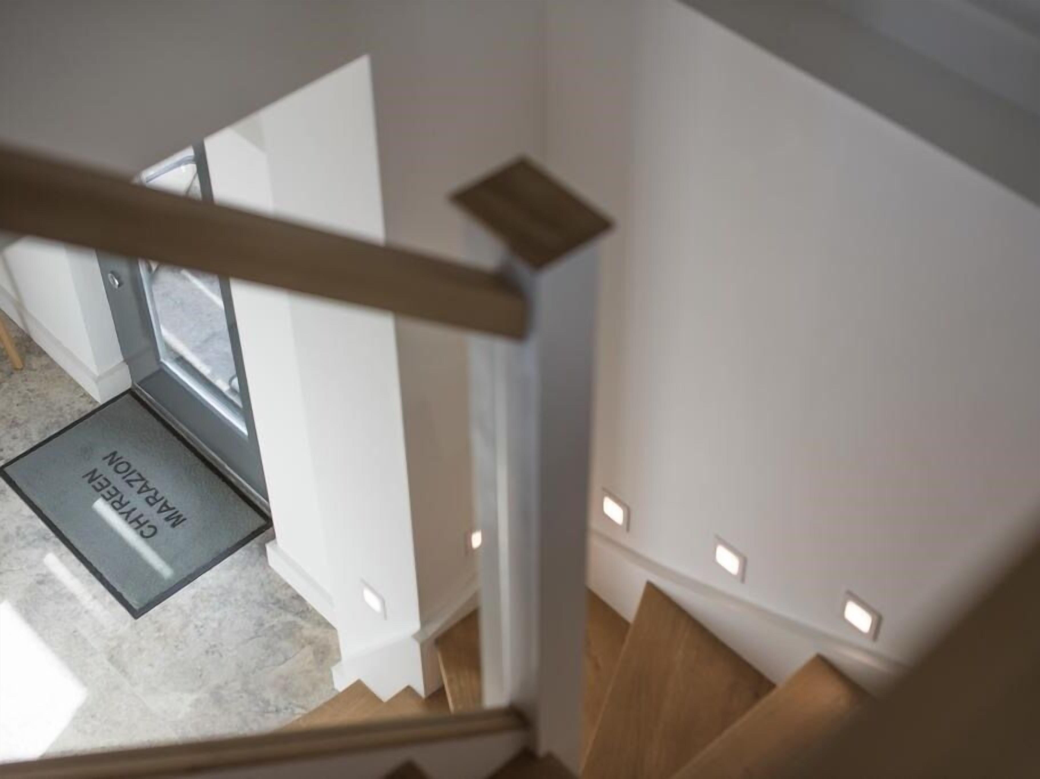 A modern staircase with a wooden handrail and a glass door leading to a room.