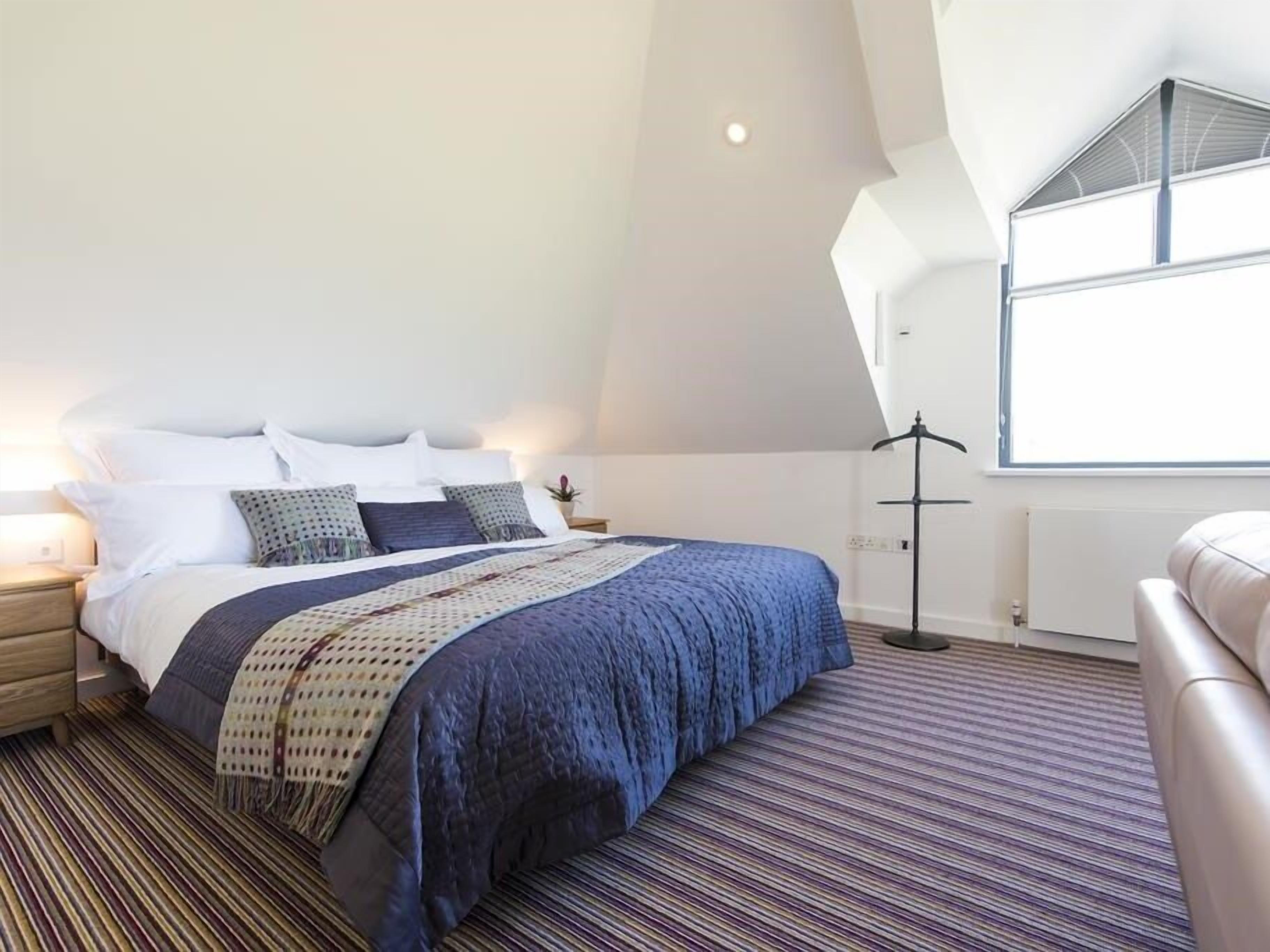 Ein modernes Schlafzimmer mit einem großen Bett, einer Stehlampe und Blick zum Himmel durch ein Dachfenster.