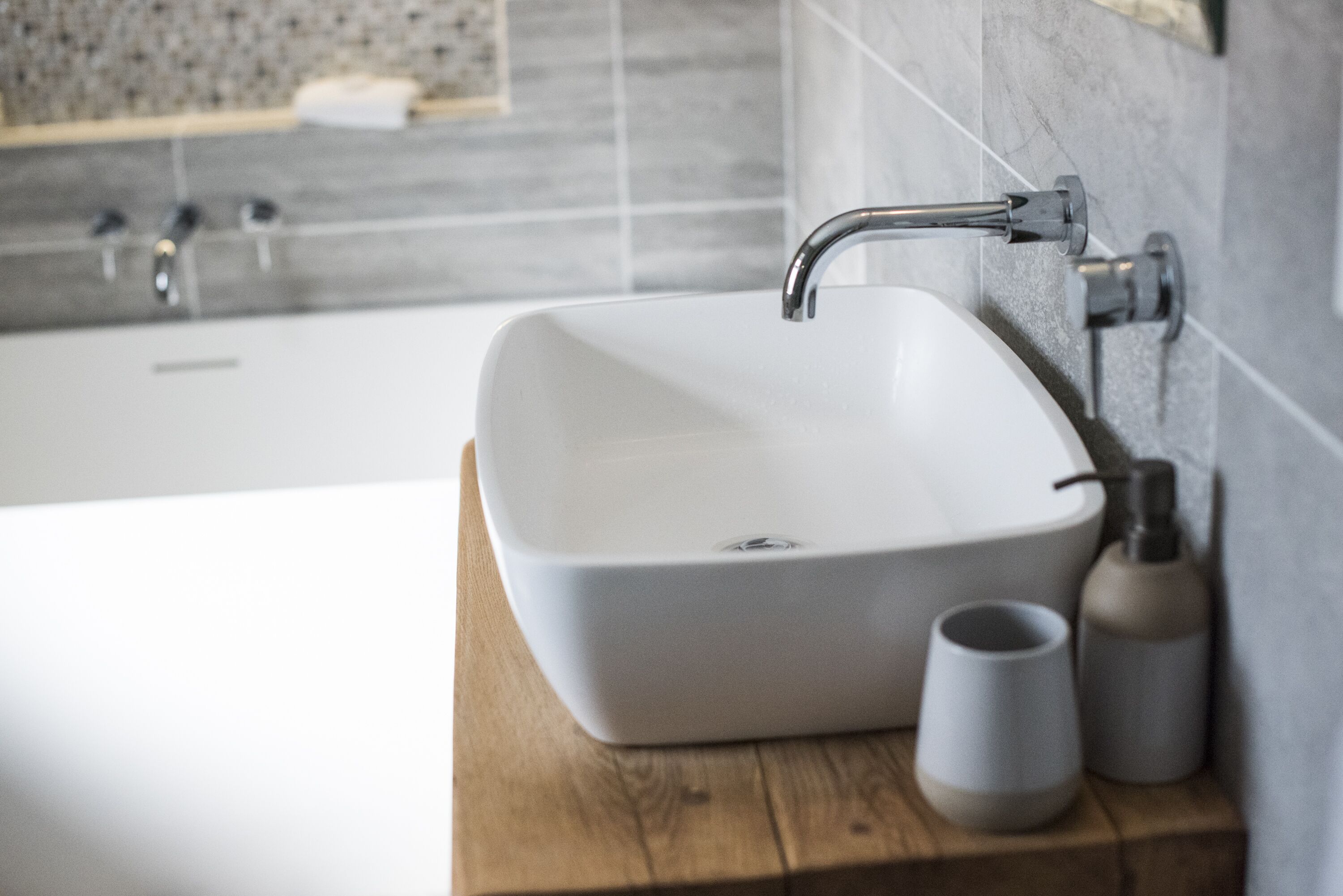 Un baño con un lavamanos blanco, una encimera de madera y una bañera al fondo.