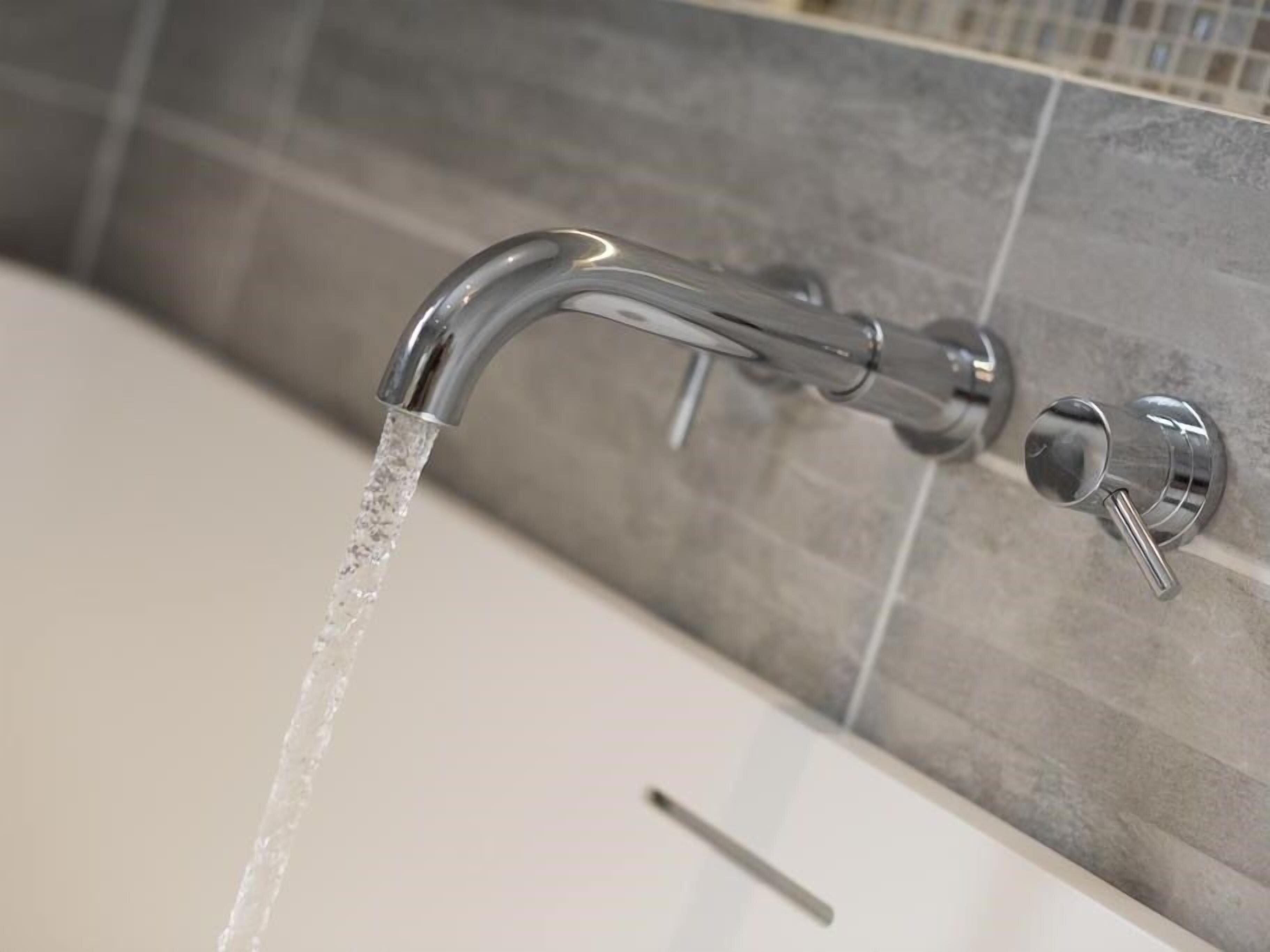 A modern bathroom with a chrome faucet and a tiled wall.