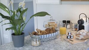 A kitchen counter with a potted plant, a basket of bread, a glass of orange juice, and a loaf of bread. - Chyreen@marazion (Marazion)