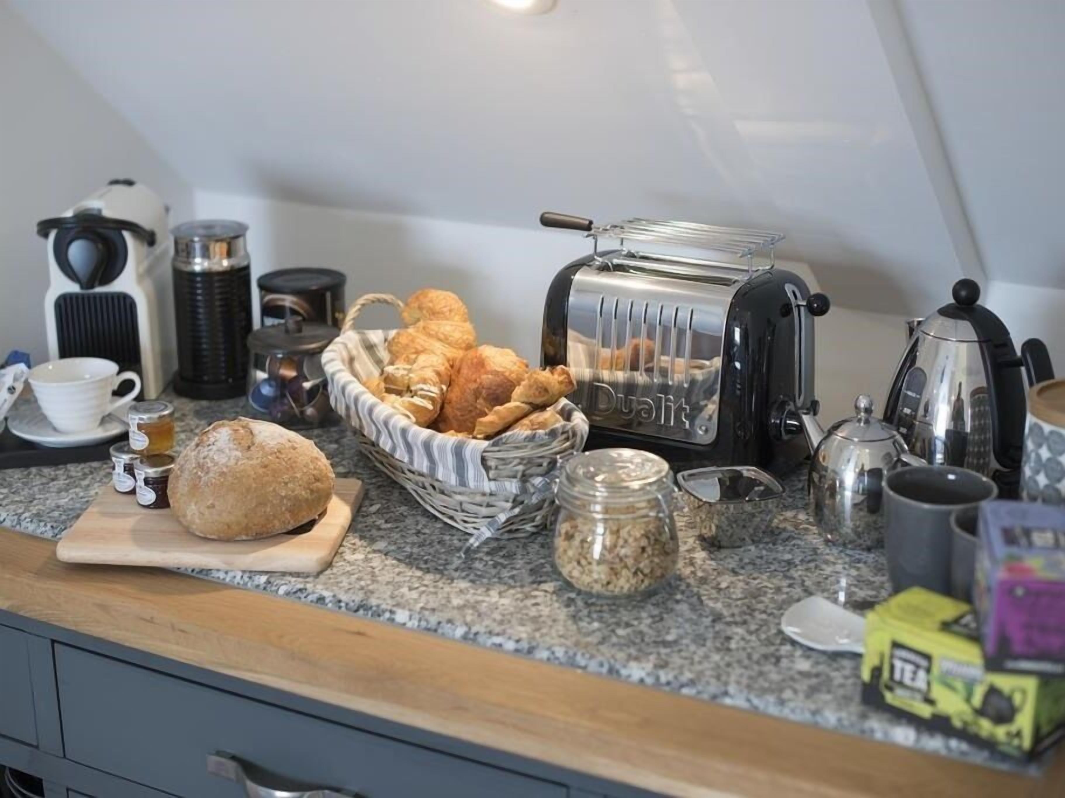 Una encimera de cocina con un tostador, una cesta de croissants, un tarro de avena y una caja de té.