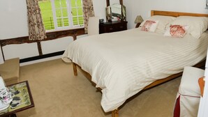 Een slaapkamer met een groot bed, een houten hoofdbord, een nachtkastje, een spiegel en een raam met bloemen gordijnen.