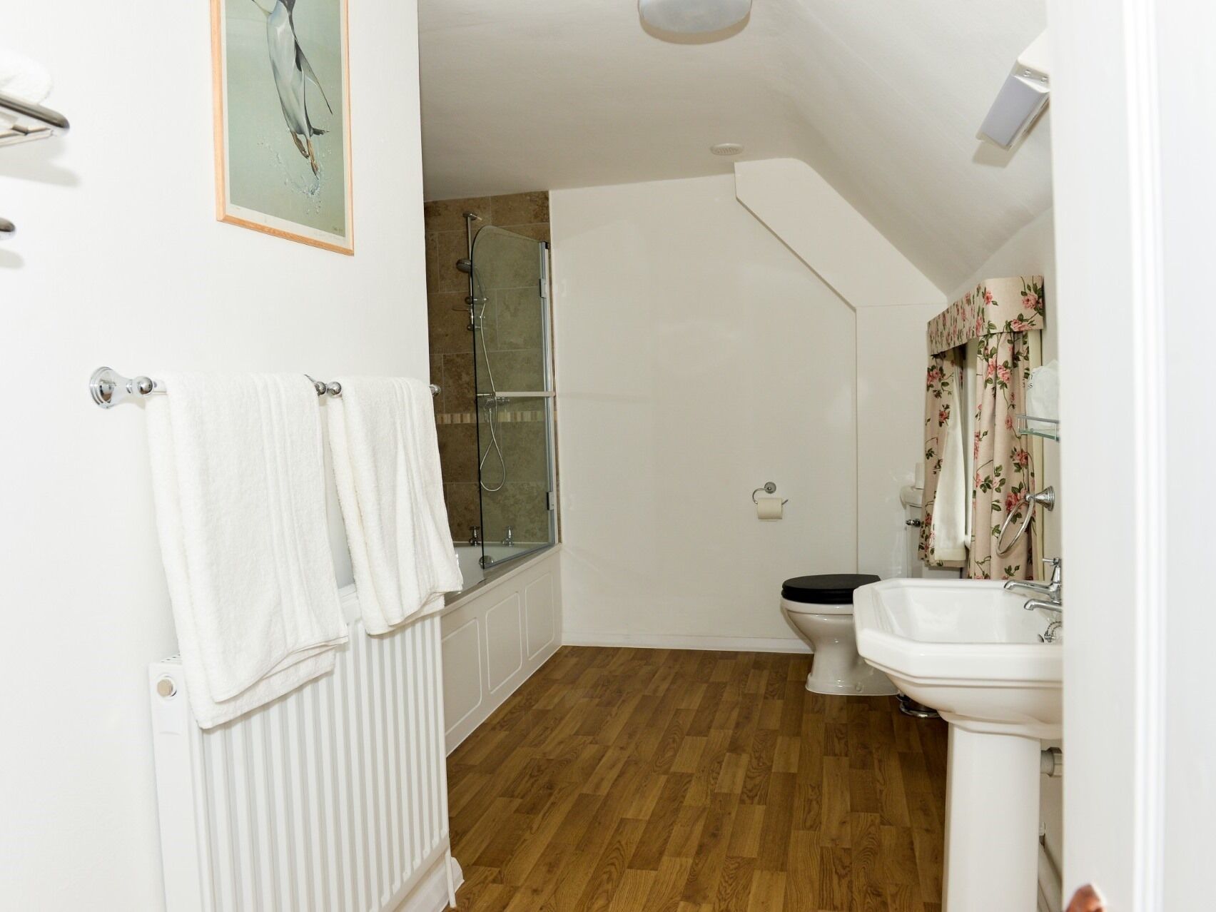 A bathroom with a wooden floor, a white radiator, a toilet, a sink, and a shower.