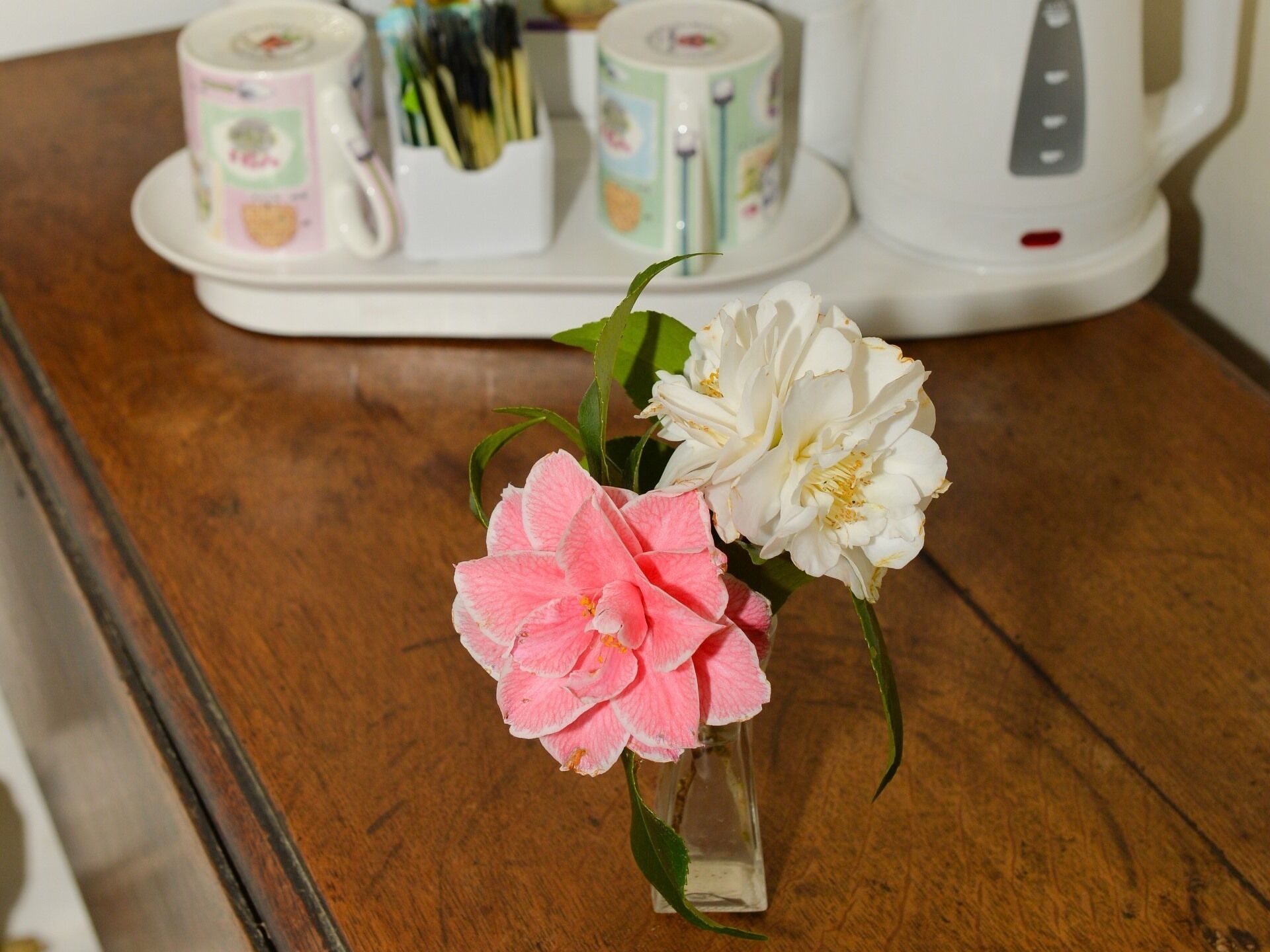 Una mesa de madera con un florero de vidrio transparente que contiene flores rosas y blancas.