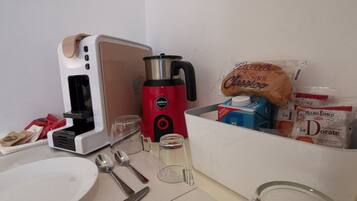 Een aanrecht met een koffiezetapparaat, een glas, een bord, bestek en enkele verpakte etenswaren.