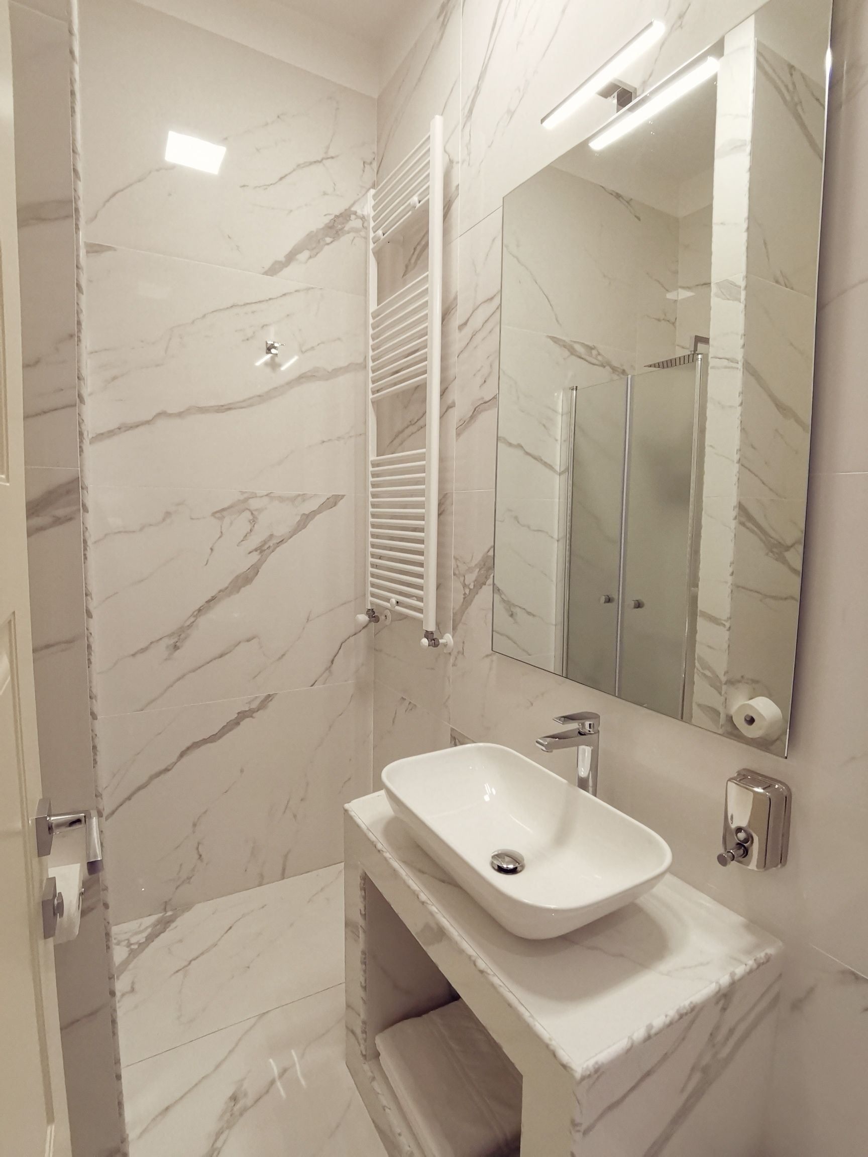 Um banheiro moderno com piso de mármore, uma pia branca com cuba única, um espelho acima da pia e um porta-toalhas.