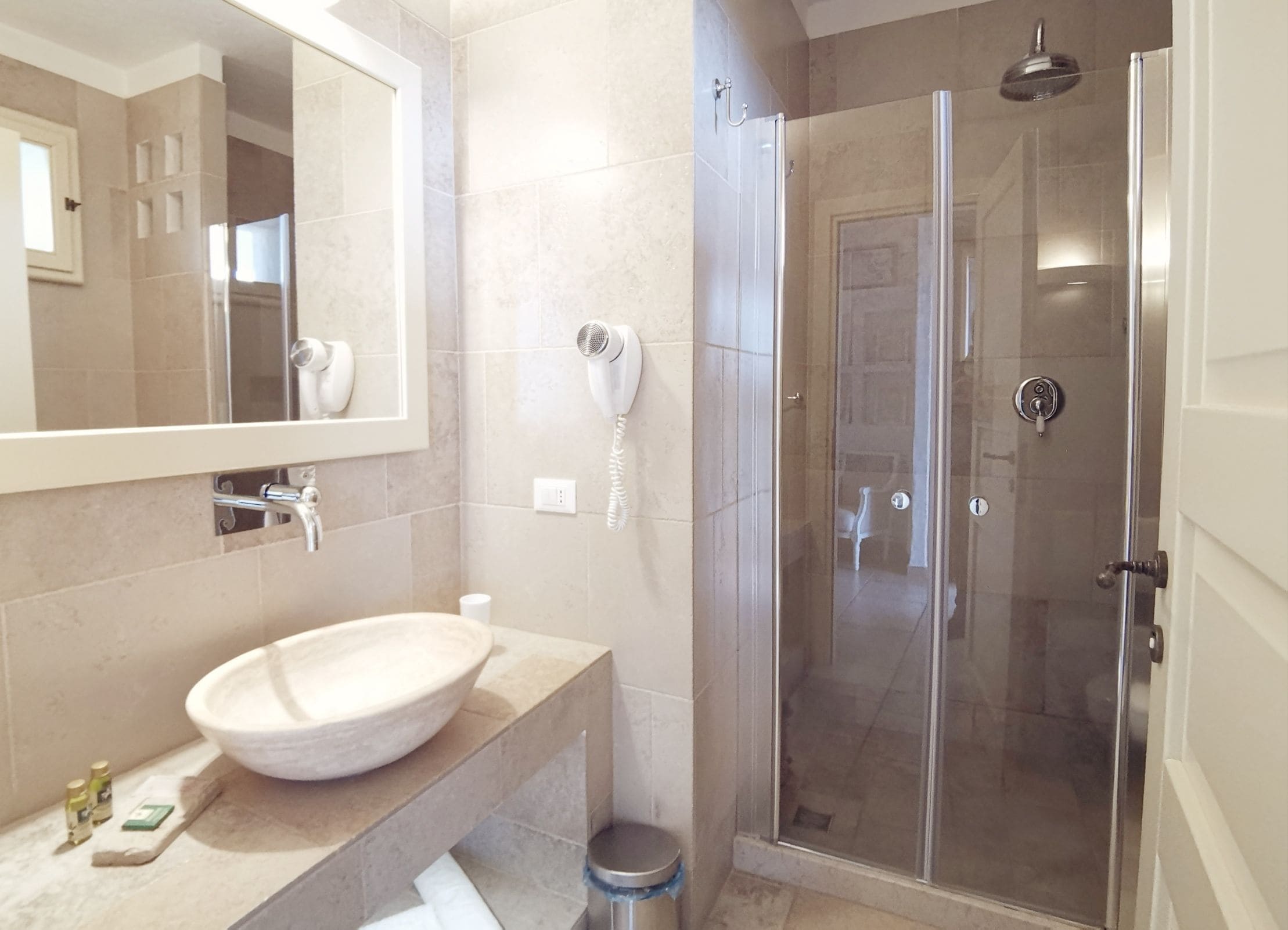 Un baño con un espejo grande, un lavabo blanco, un secador de pelo de mano y una ducha con mampara de vidrio.