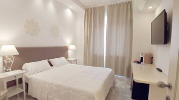 Une chambre d’hôtel avec un lit, des tables de chevet, un bureau, une télévision et une fenêtre avec des rideaux.