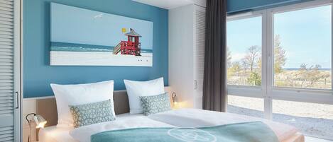 A bedroom with a large bed, a view of the beach, and a lifeguard tower painting on the wall.