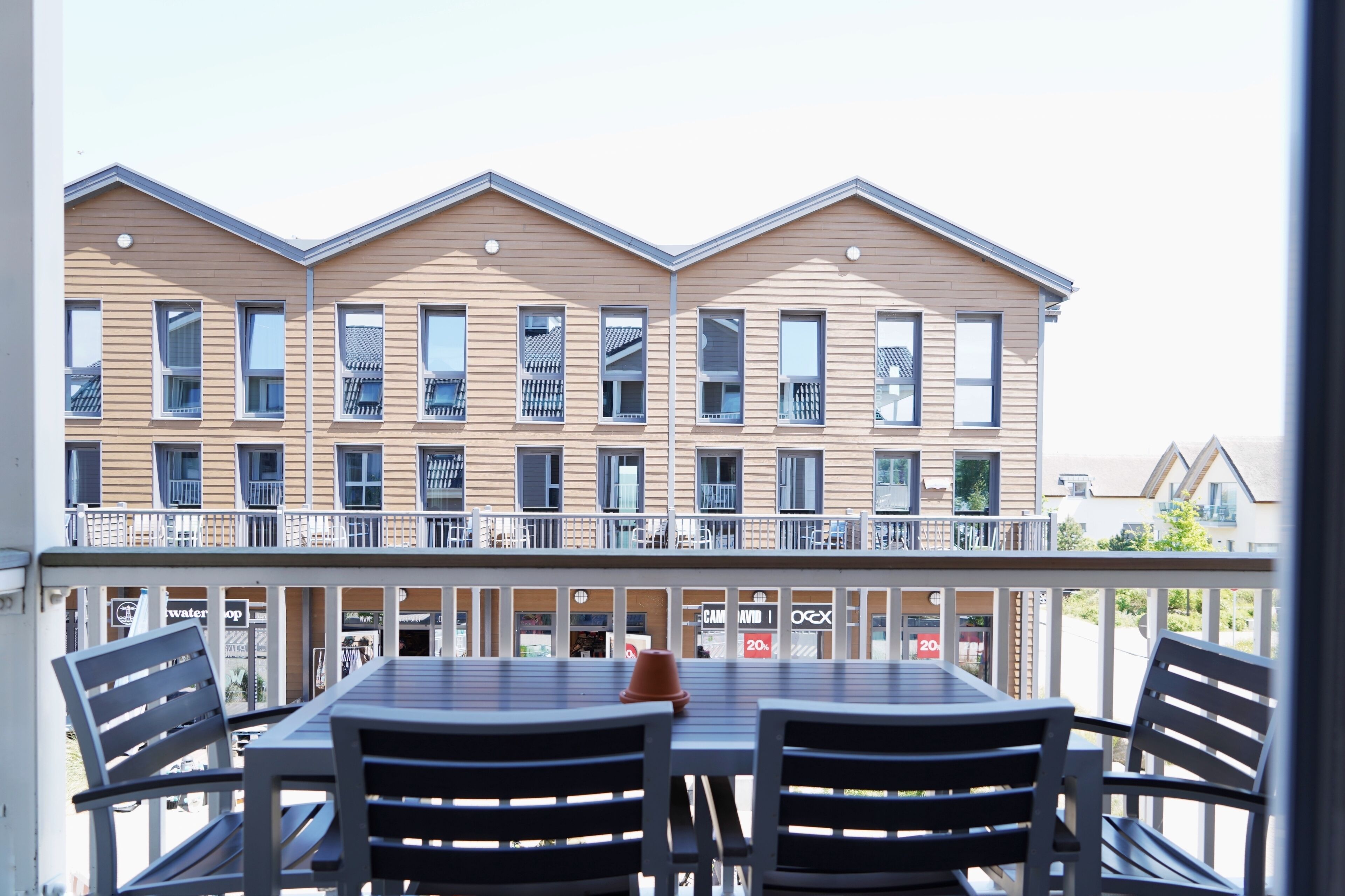 A balcony with a table and chairs, overlooking a row of buildings with balconies.