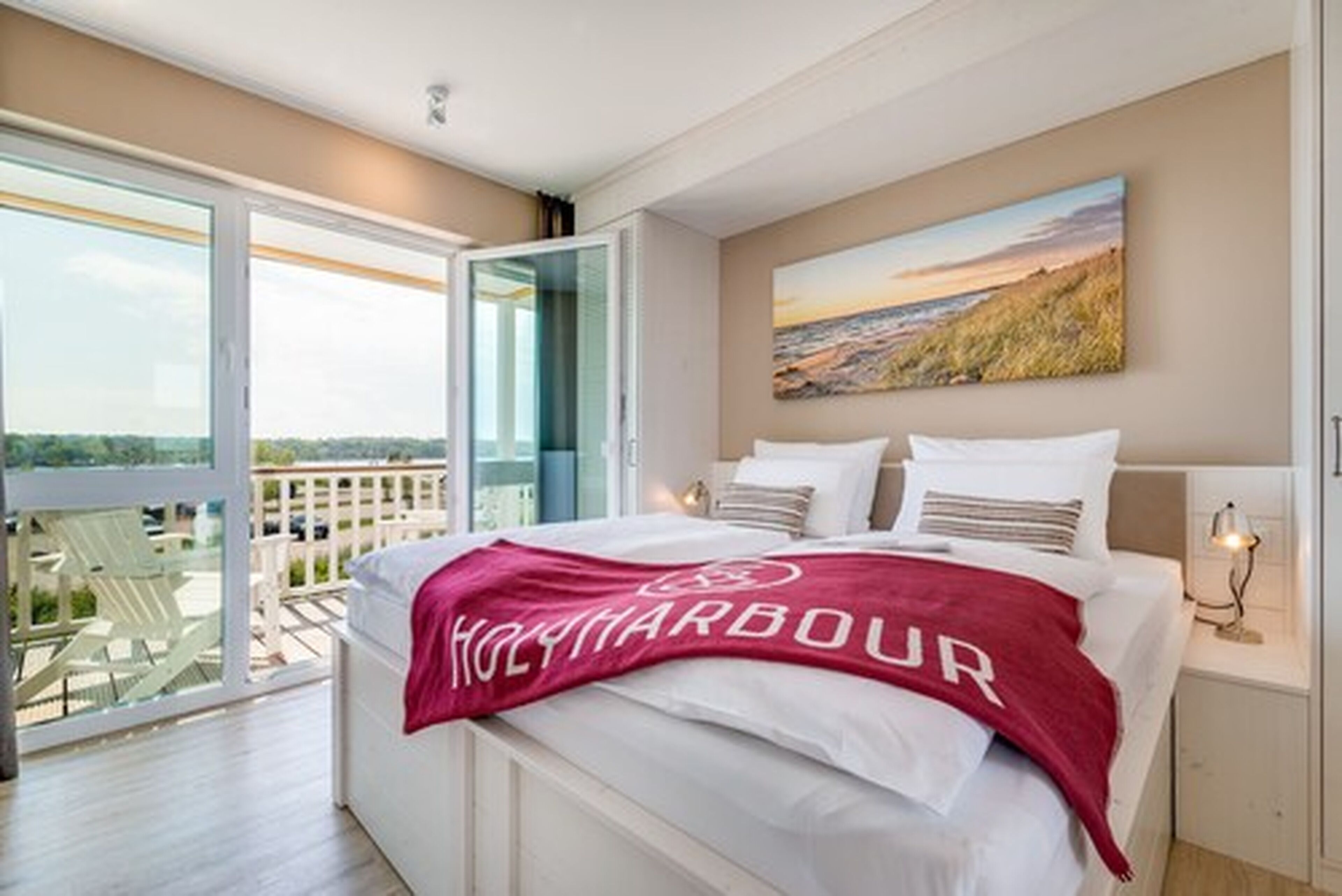 A hotel room with a large bed, a balcony with outdoor furniture, and a scenic view.