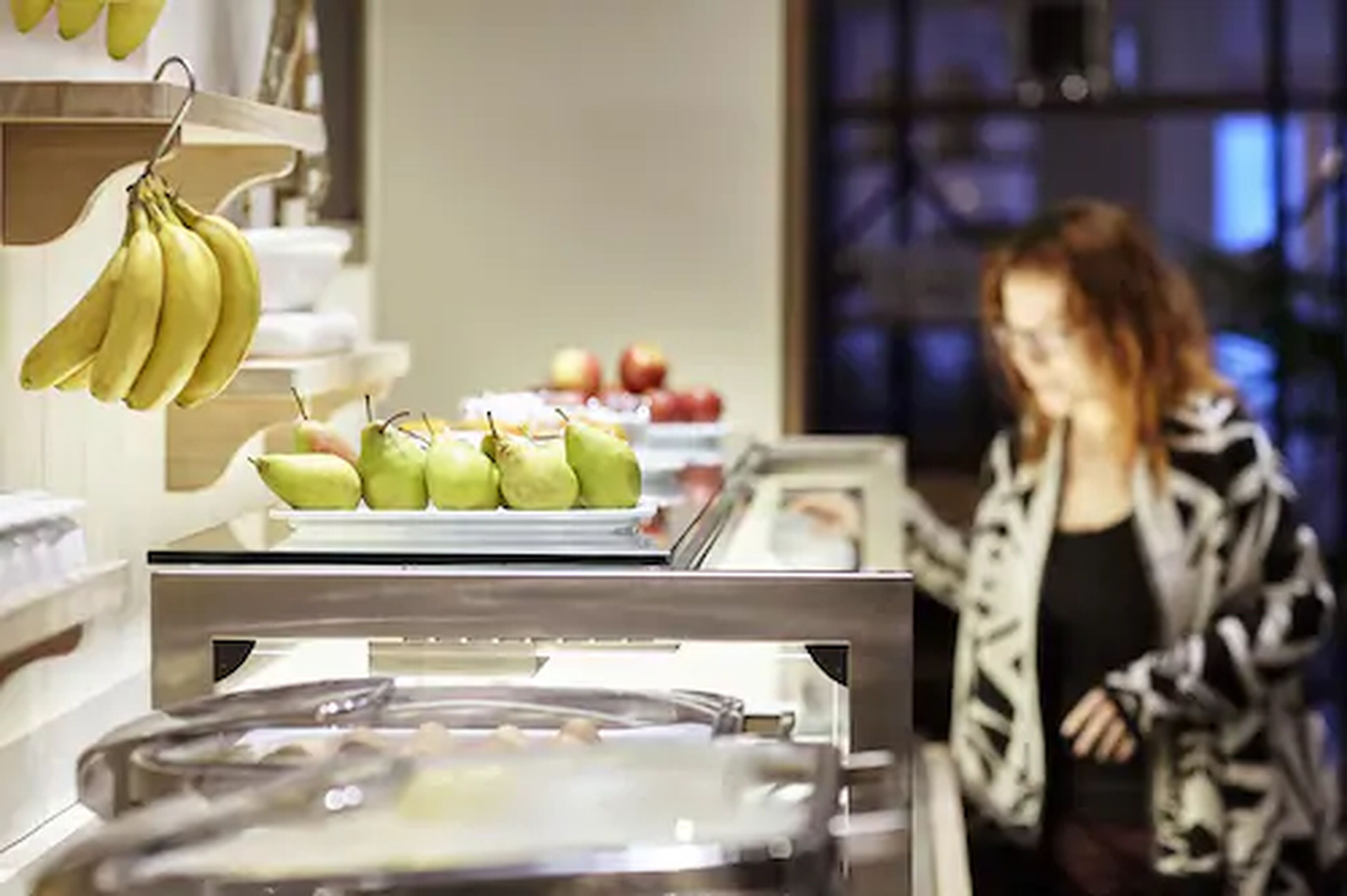 A buffet area with various fruits like bananas and pears, and a person in the background.