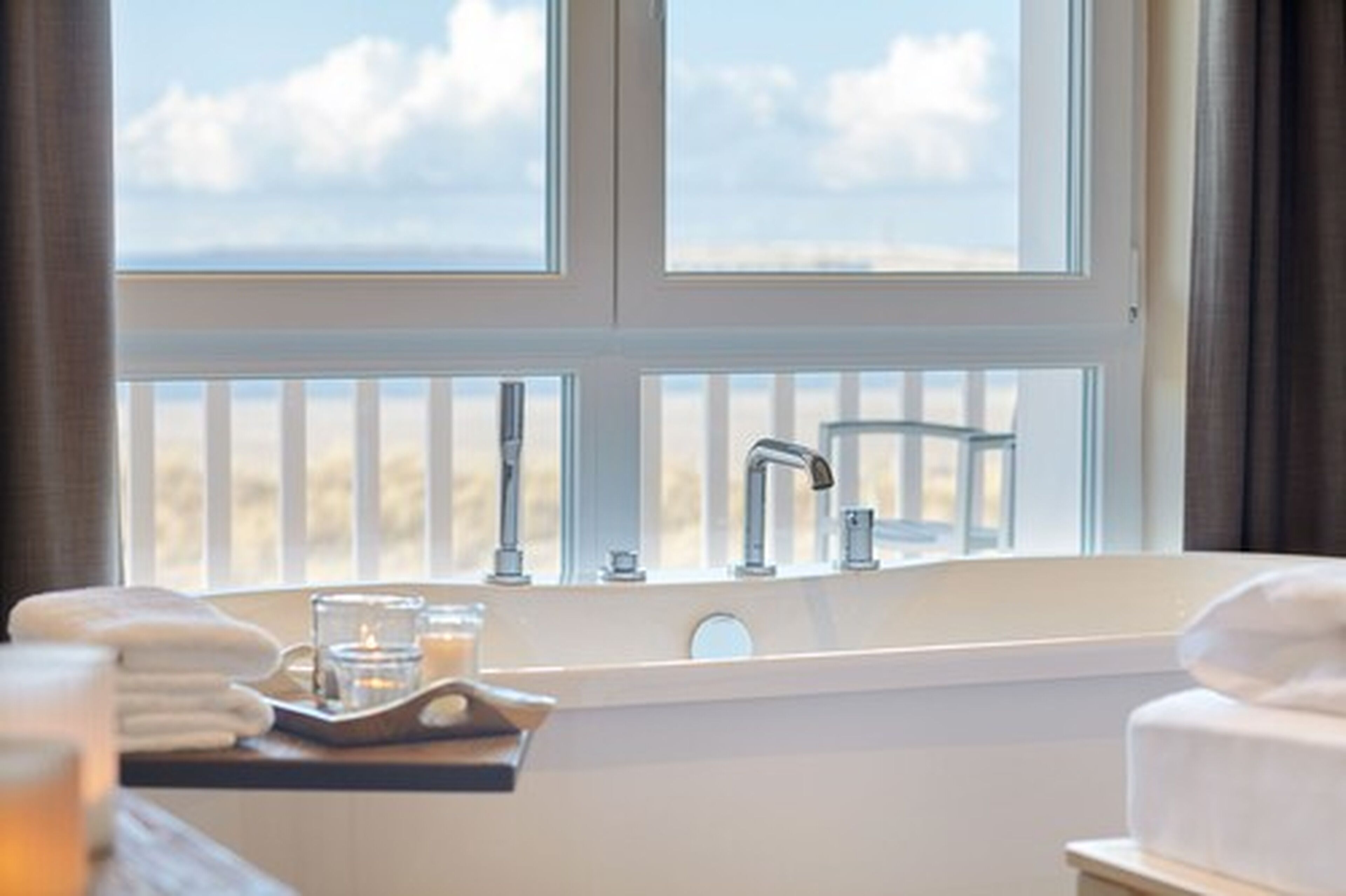 A bathroom with a large window, a sink, and a tray with towels and candles.