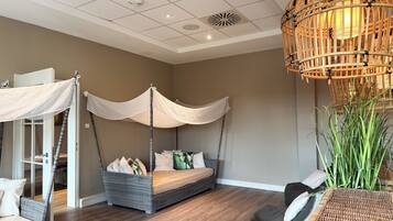 Un dormitorio con cama a dosel, sofá de mimbre, lámpara de ratán y una planta grande.
