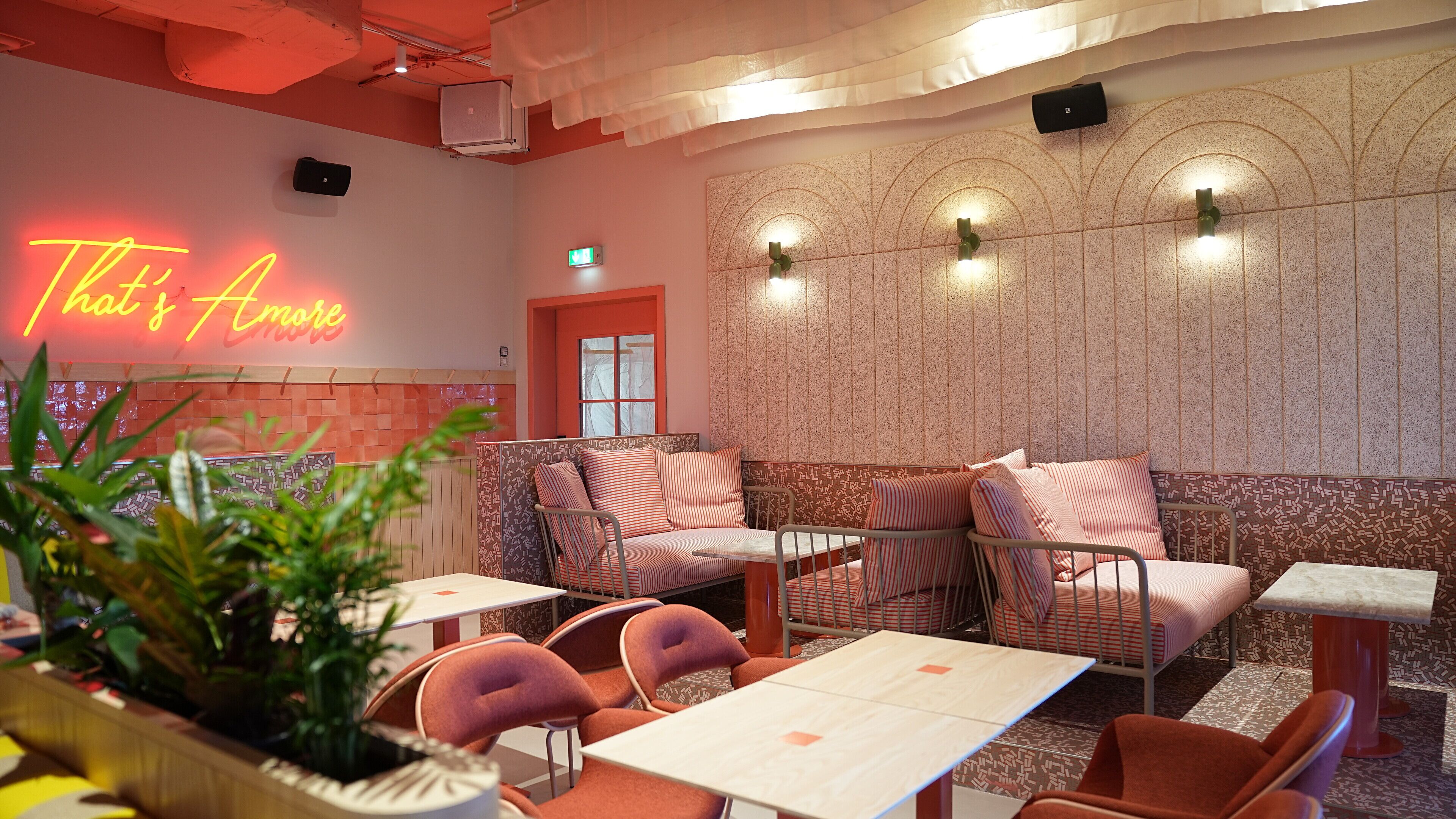 A cozy restaurant interior with a neon sign, patterned walls, and comfortable seating.