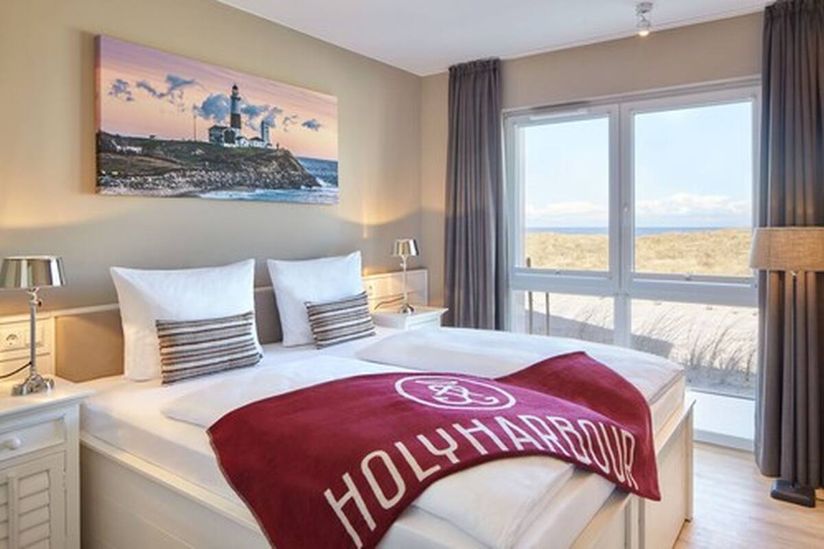Une chambre d’hôtel avec un grand lit, une vue sur la plage et un tableau représentant un phare.