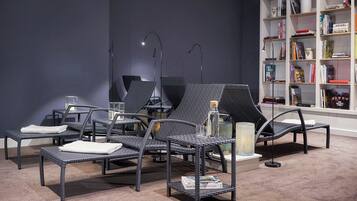 Relax in a serene space with wicker lounge chairs and a floor lamp, surrounded by a bookshelf filled with books.