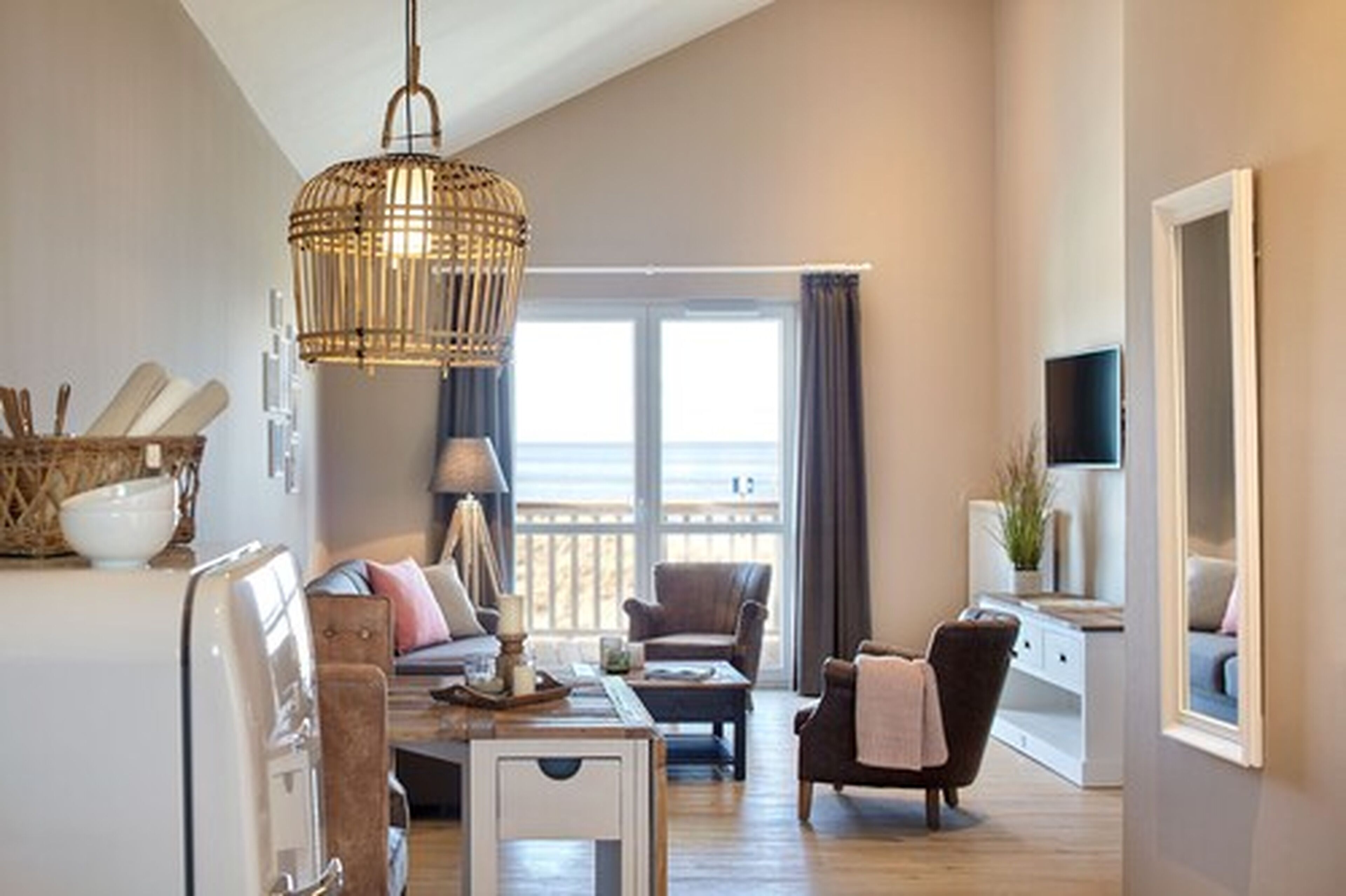 A spacious living room with a large window, a wicker chandelier, and a cozy seating area.