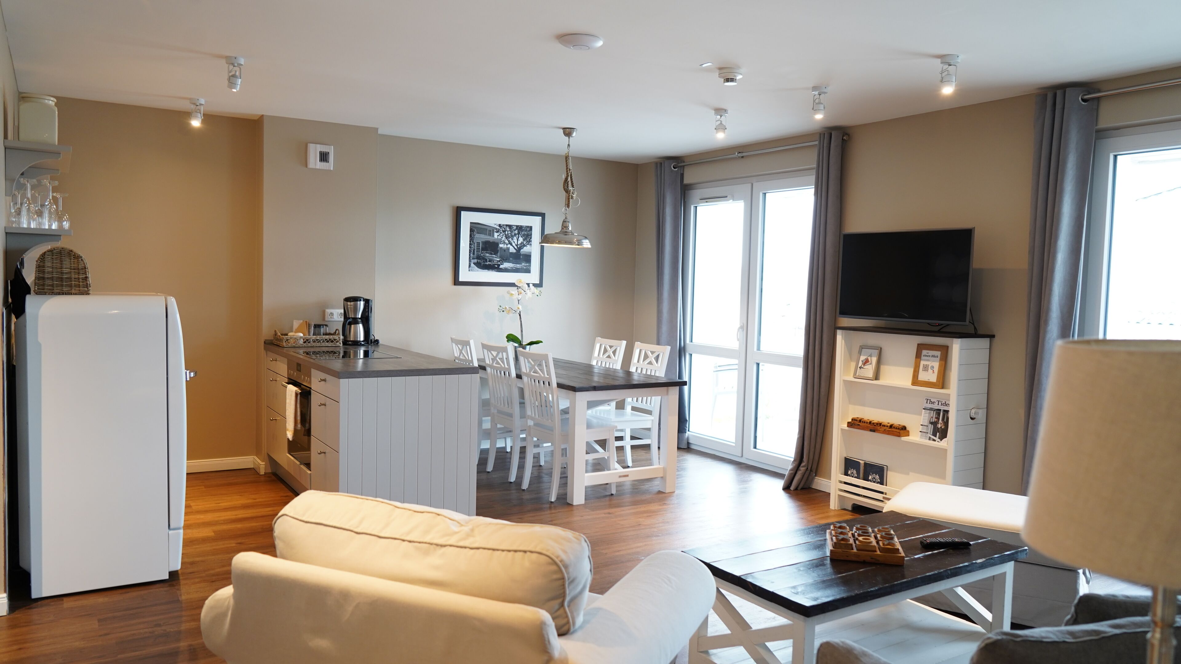 Eine moderne Wohnung mit Küche, Essbereich und Wohnzimmer. Sie umfasst einen Kühlschrank, eine Kaffeemaschine, einen Esstisch und Stühle.