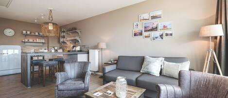 A modern living room with a grey sofa, two armchairs, a coffee table, and a kitchen area in the background.