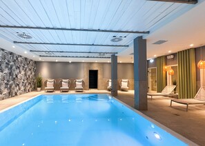 Una piscina interior moderna con sillas de descanso y una pared de piedra.