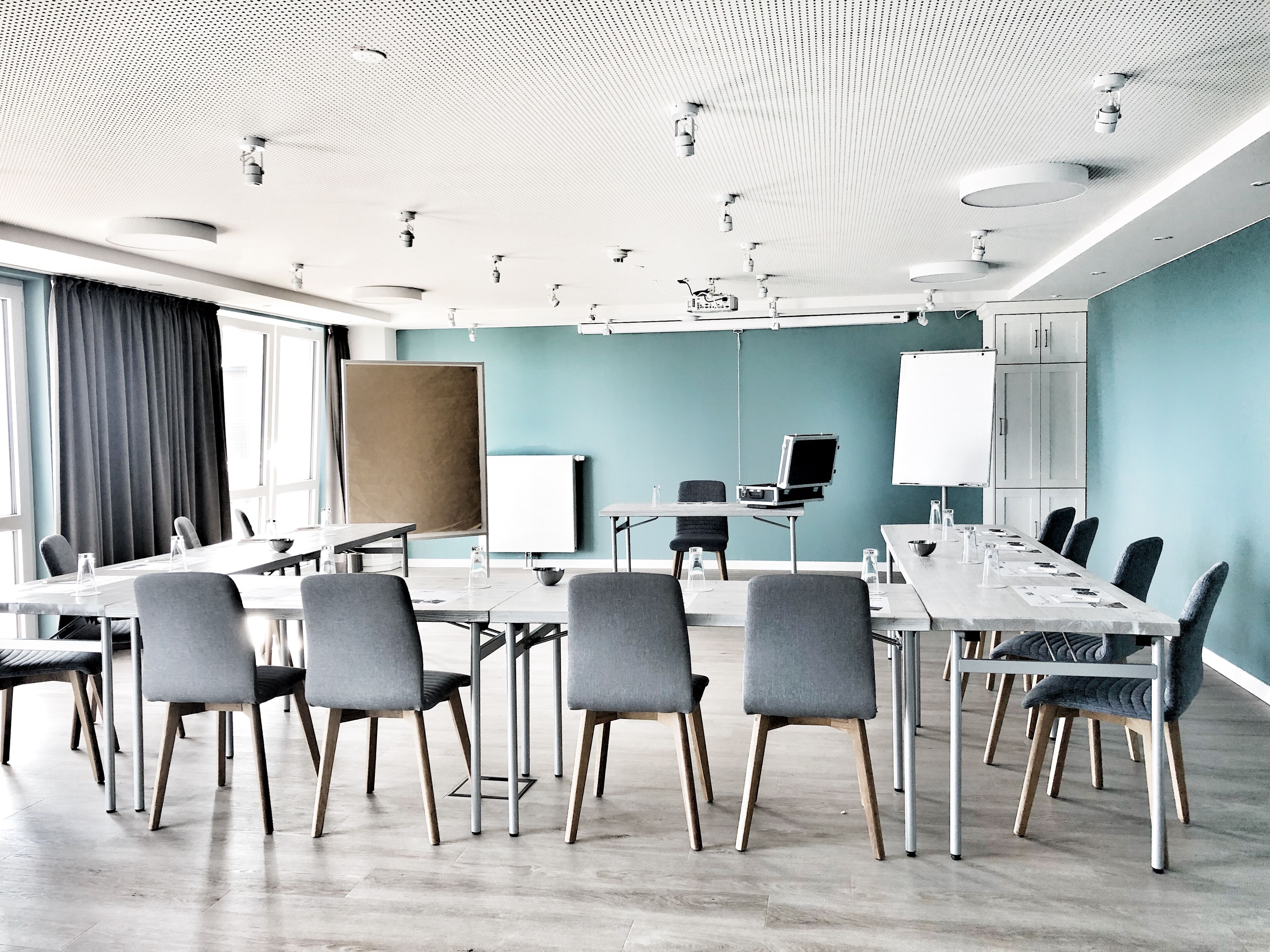 Una sala conferenze moderna con un lungo tavolo, sedie grigie, una lavagna e un proiettore.