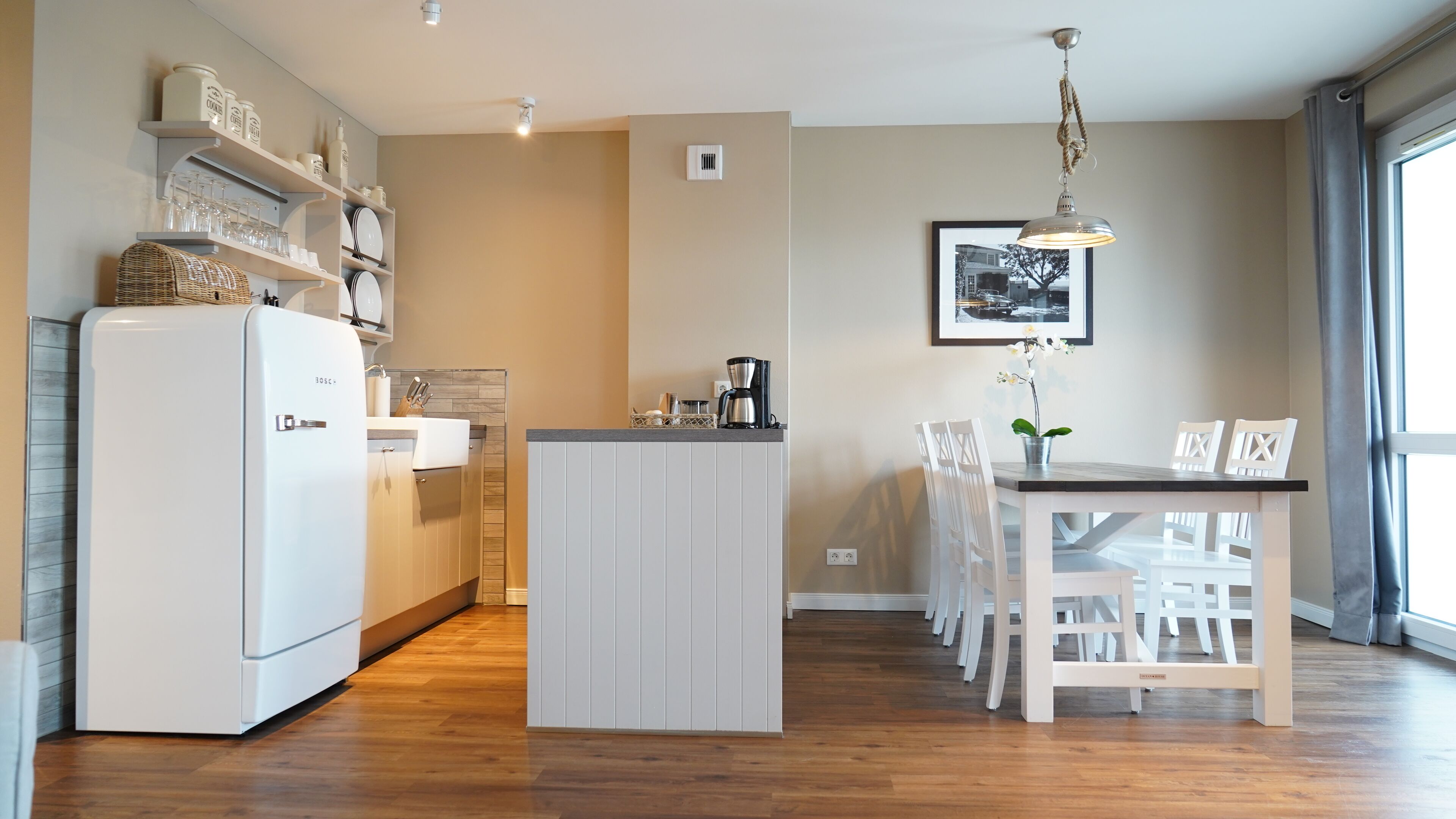 A modern kitchen with white cabinets, a built-in island, and a dining area with white chairs.