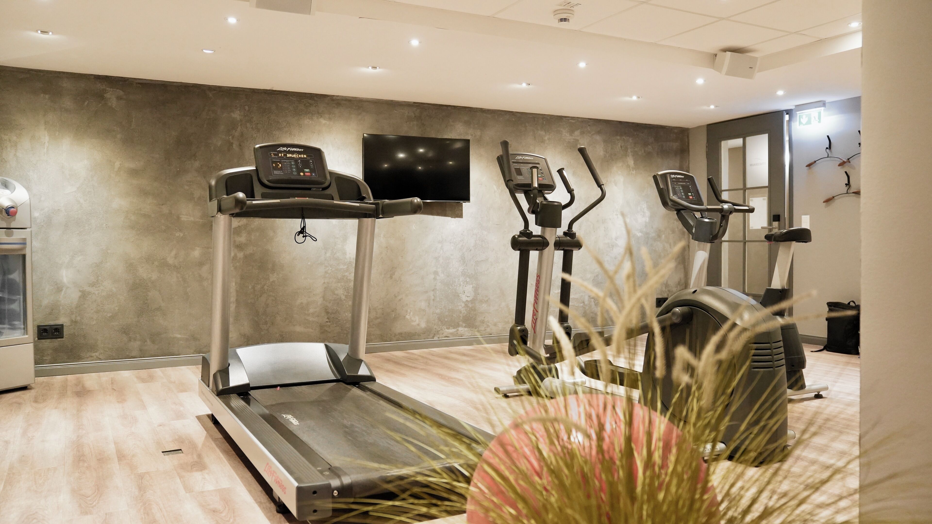 A gym with treadmills and exercise equipment, a water dispenser, and a television on the wall.