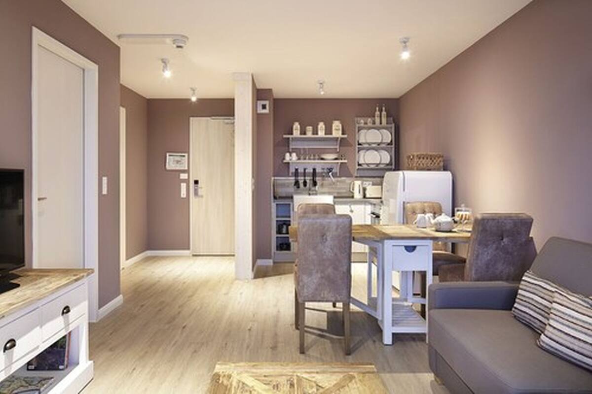 Un salon moderne comprenant un canapé, une table à manger avec des chaises et un coin cuisine avec des étagères et des appareils électroménagers.