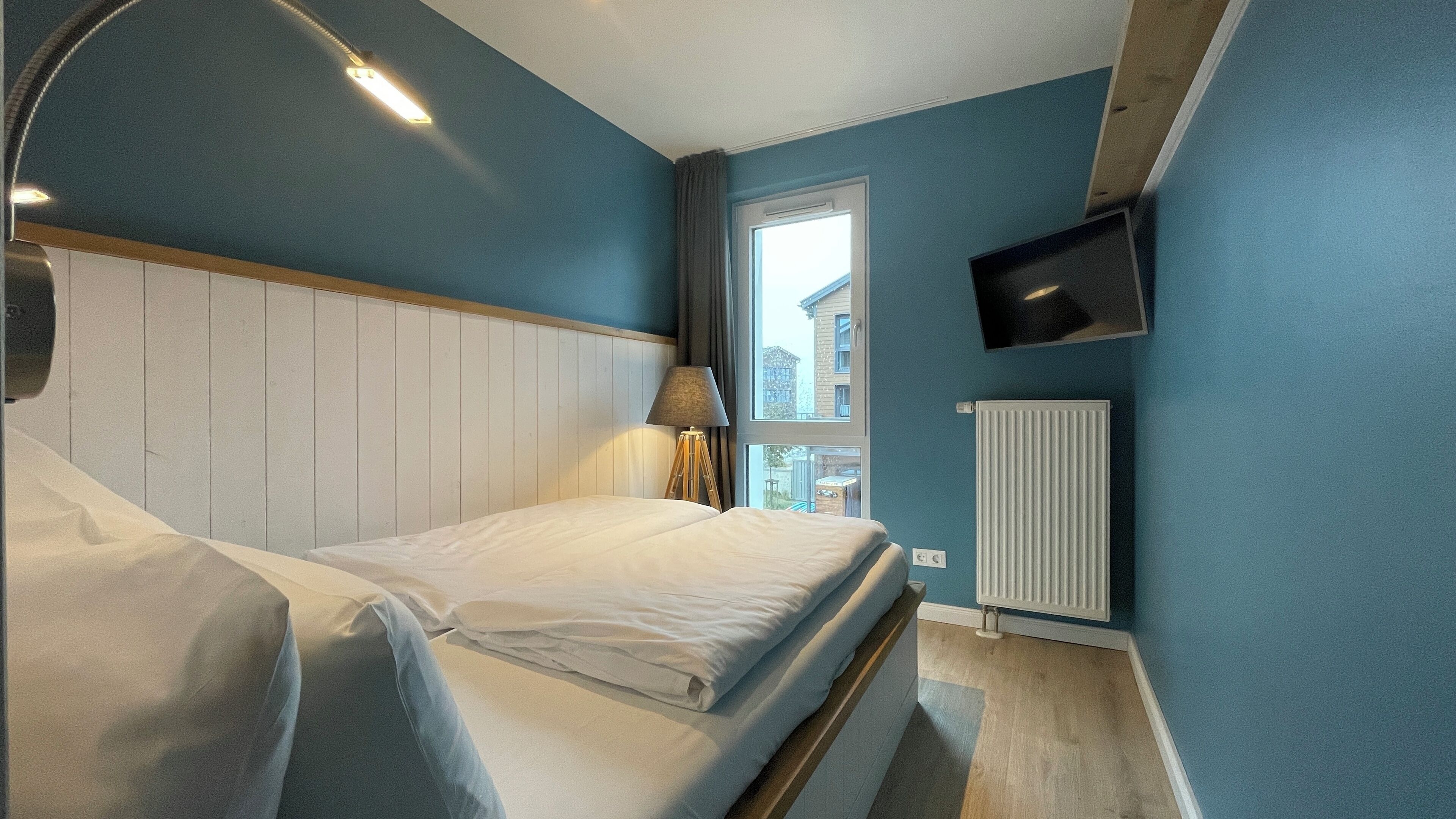 A bedroom with a bed, a lamp, a TV, and a window with a view of buildings.