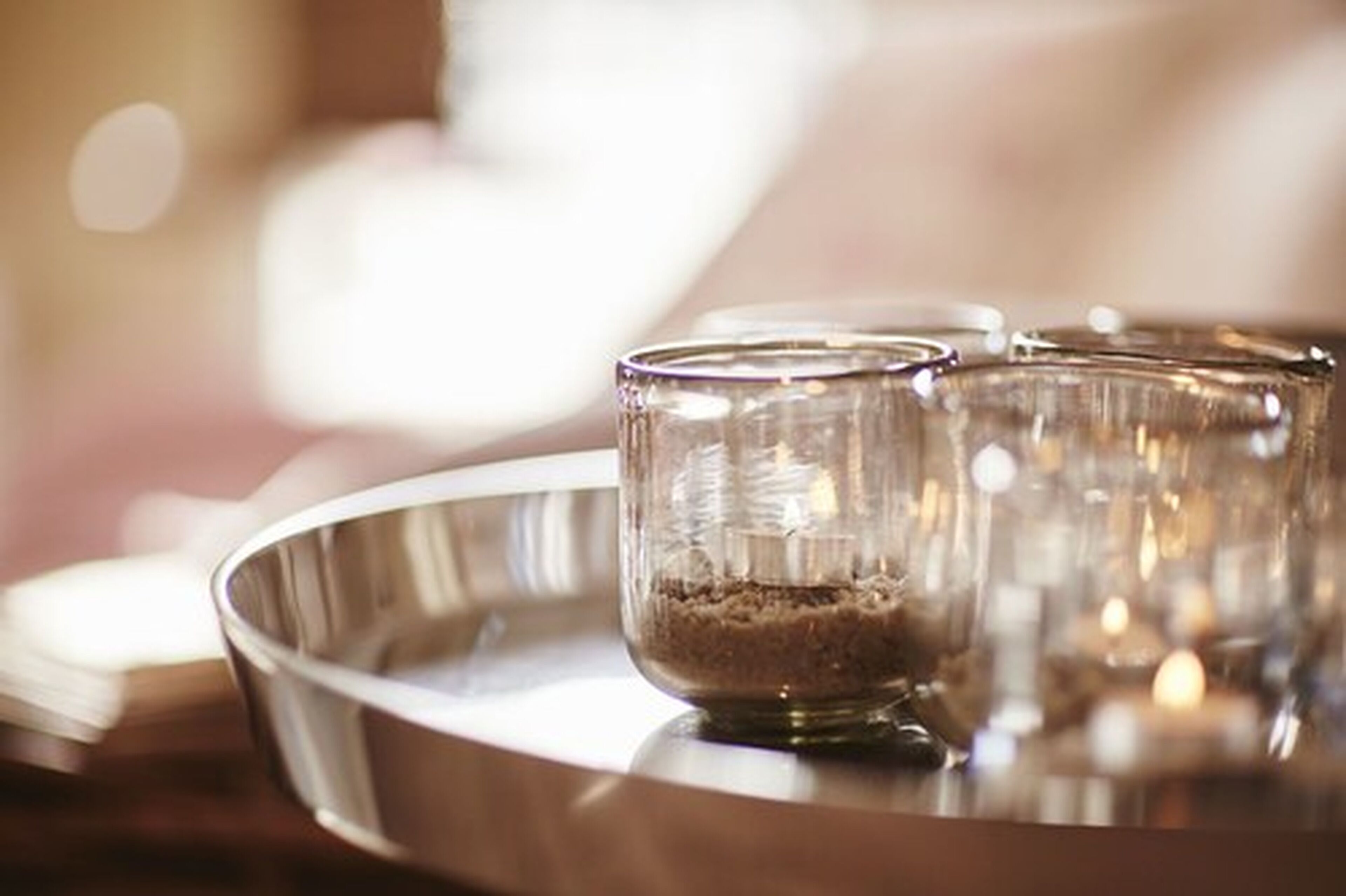 A metallic tray with a glass container filled with a granular substance, possibly sugar, and a clear glass.