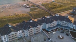 Et kysthotel med flere bygninger, en mole der strækker sig ud i havet, og et strandområde med parasoller.