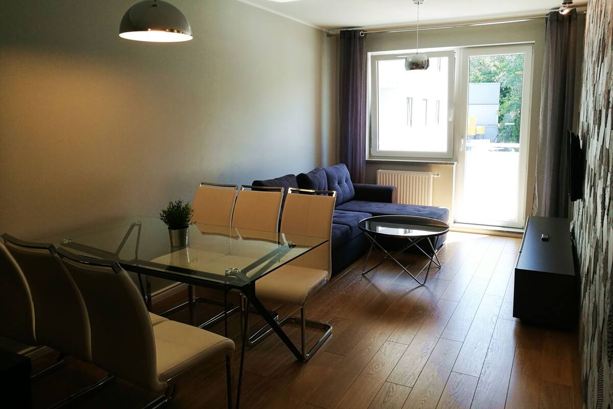 A modern living room with a glass dining table, a sofa, and a small side table.