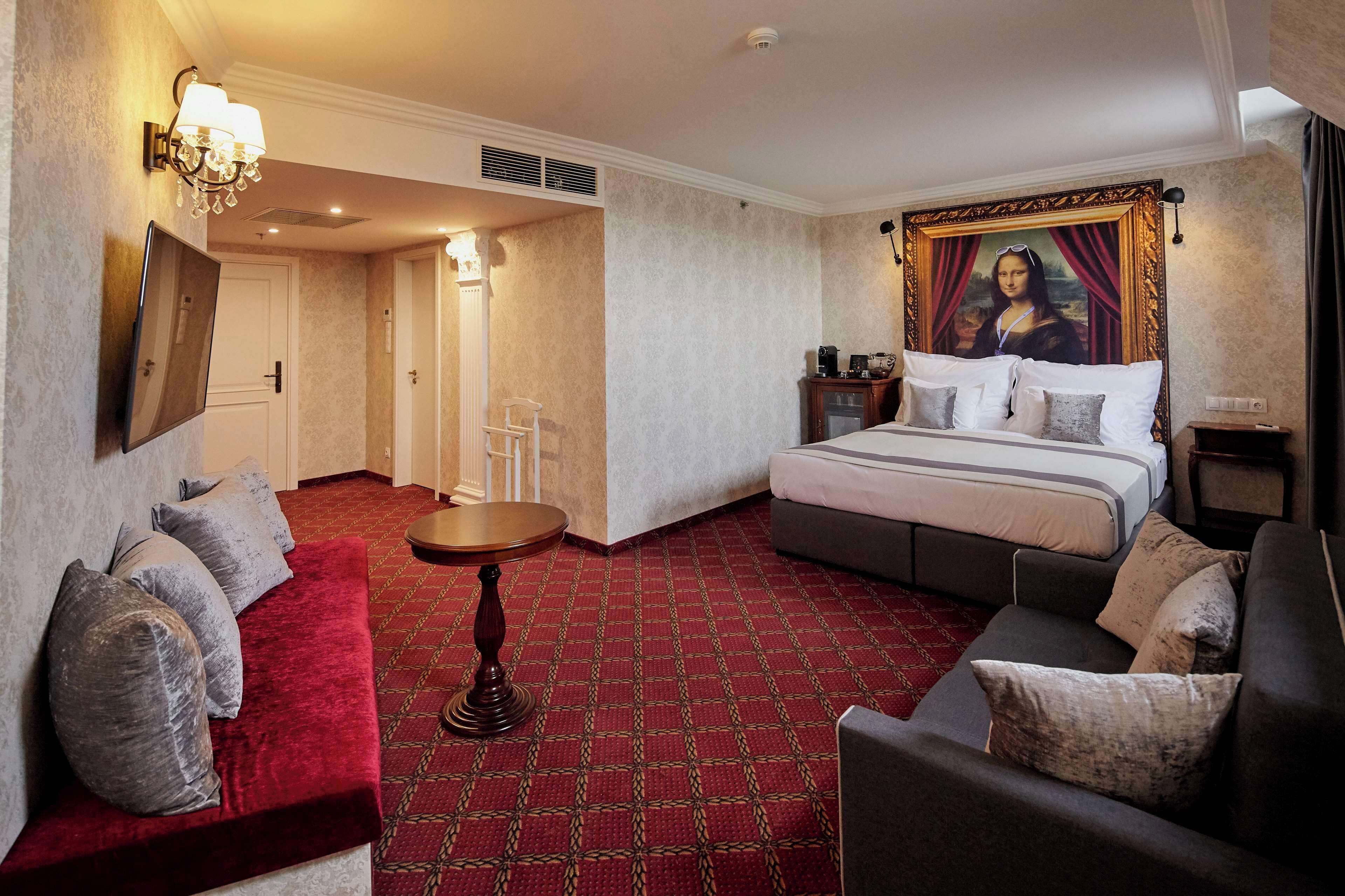 A hotel room with a large bed, a red carpet, a sofa, and a painting of the Mona Lisa on the wall.