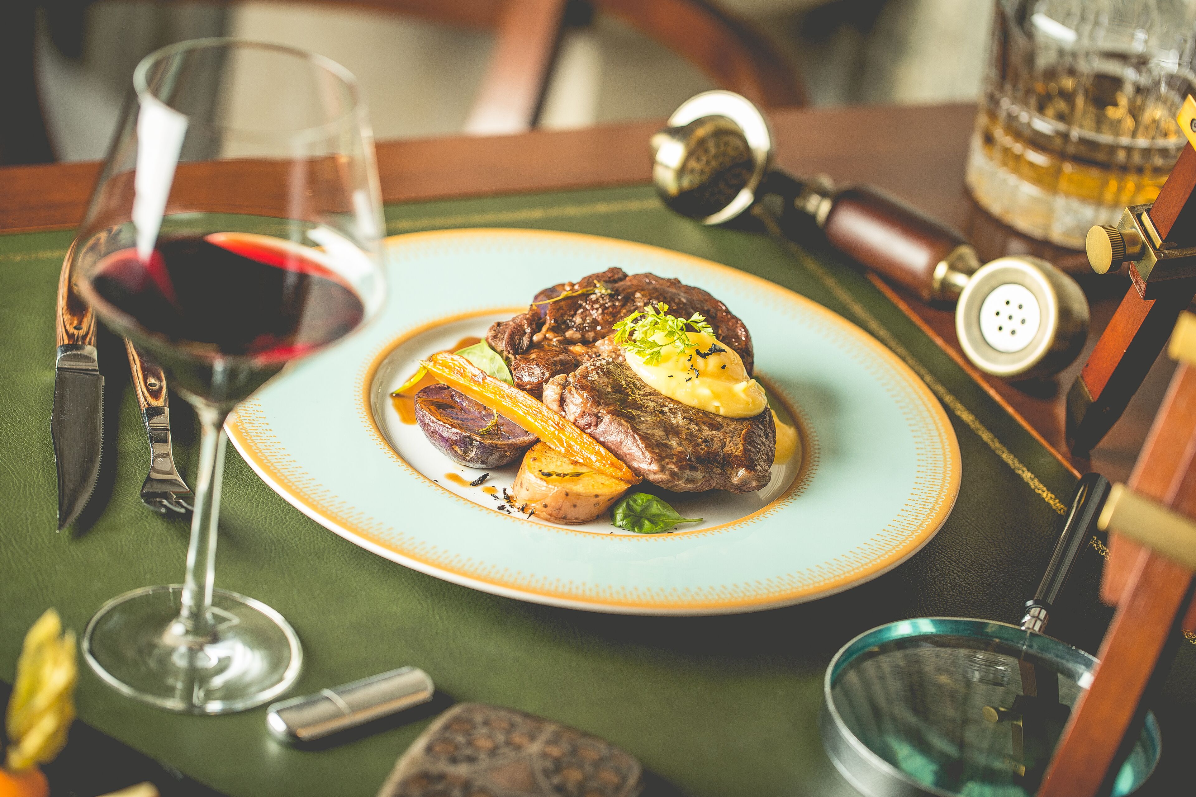 Ein Teller mit Steak, Gemüse und einem Glas Rotwein auf einem Tisch.