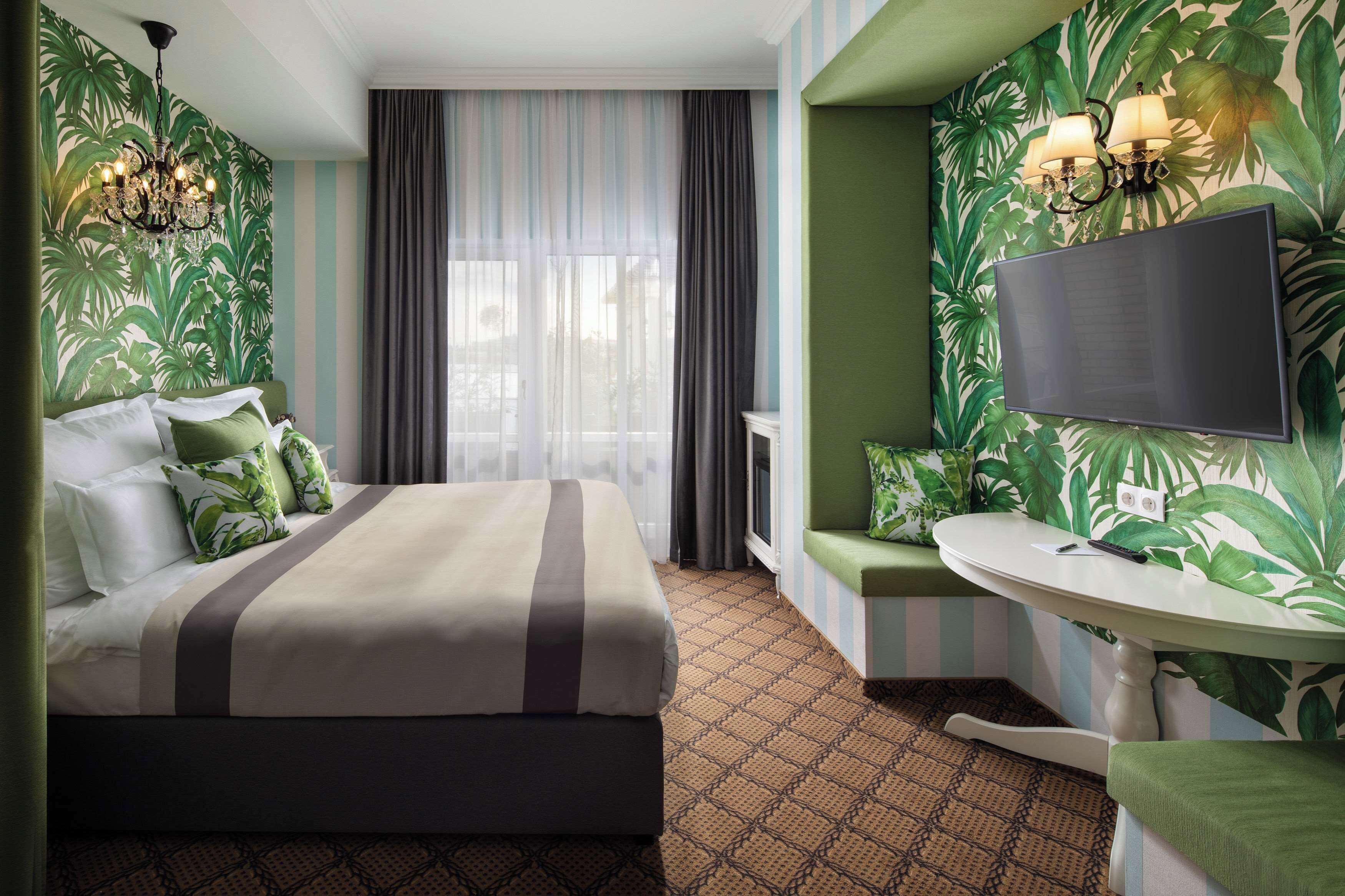 Una habitación de hotel con cama, televisión, una mesita y ventana con cortinas.