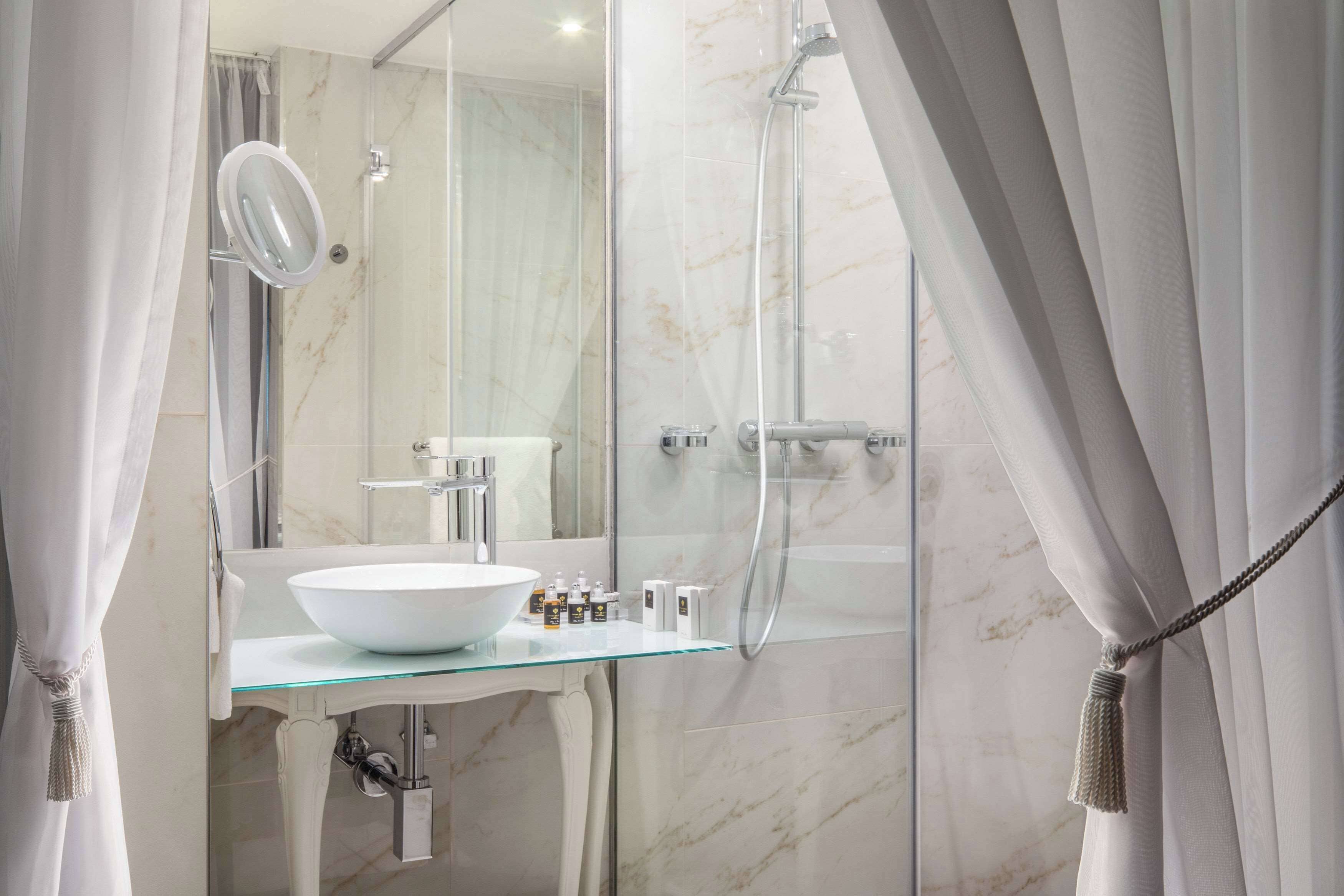 A modern bathroom with a glass sink, a large mirror, and a glass-enclosed shower.
