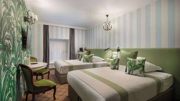 Ein Hotelzimmer mit zwei Betten, einem Schreibtisch, einem Stuhl, einer Kandelaber und gestreifter Tapete.
