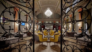 A grand dining area with ornate metal railings, a chandelier, and a bar in the background. - Mystery Hotel Budapest, Preferred Hotels & Resorts  (Budapest)
