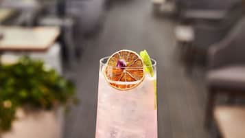 A cocktail on a table with dice and a blurred outdoor seating area in the background.