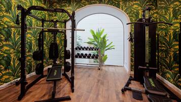 Un gimnasio con suelo de madera, equipamiento de levantamiento de pesas y una planta en el centro.