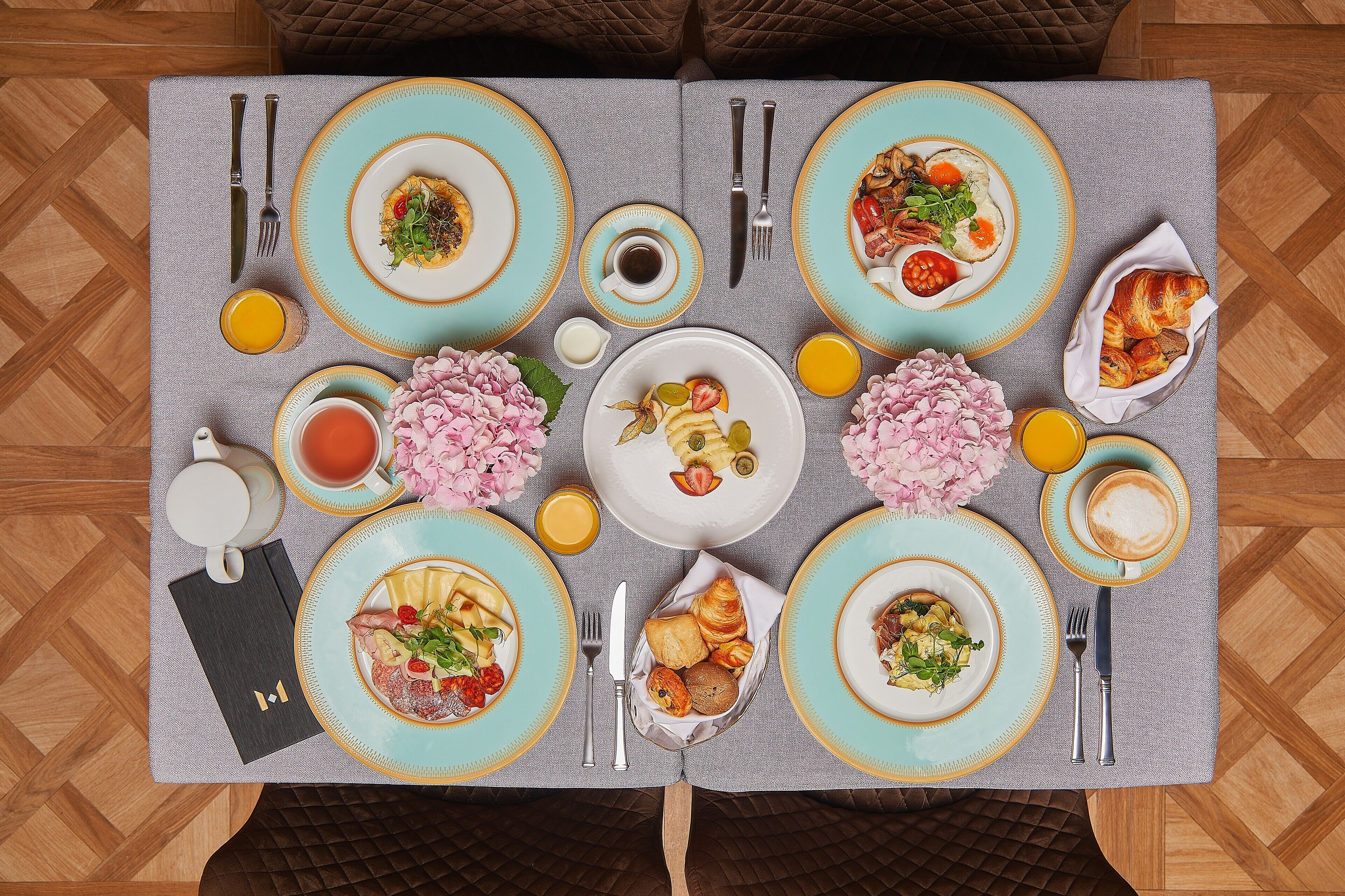 Una mesa de desayuno dispuesta con platos, cubiertos y diversos alimentos para el desayuno.