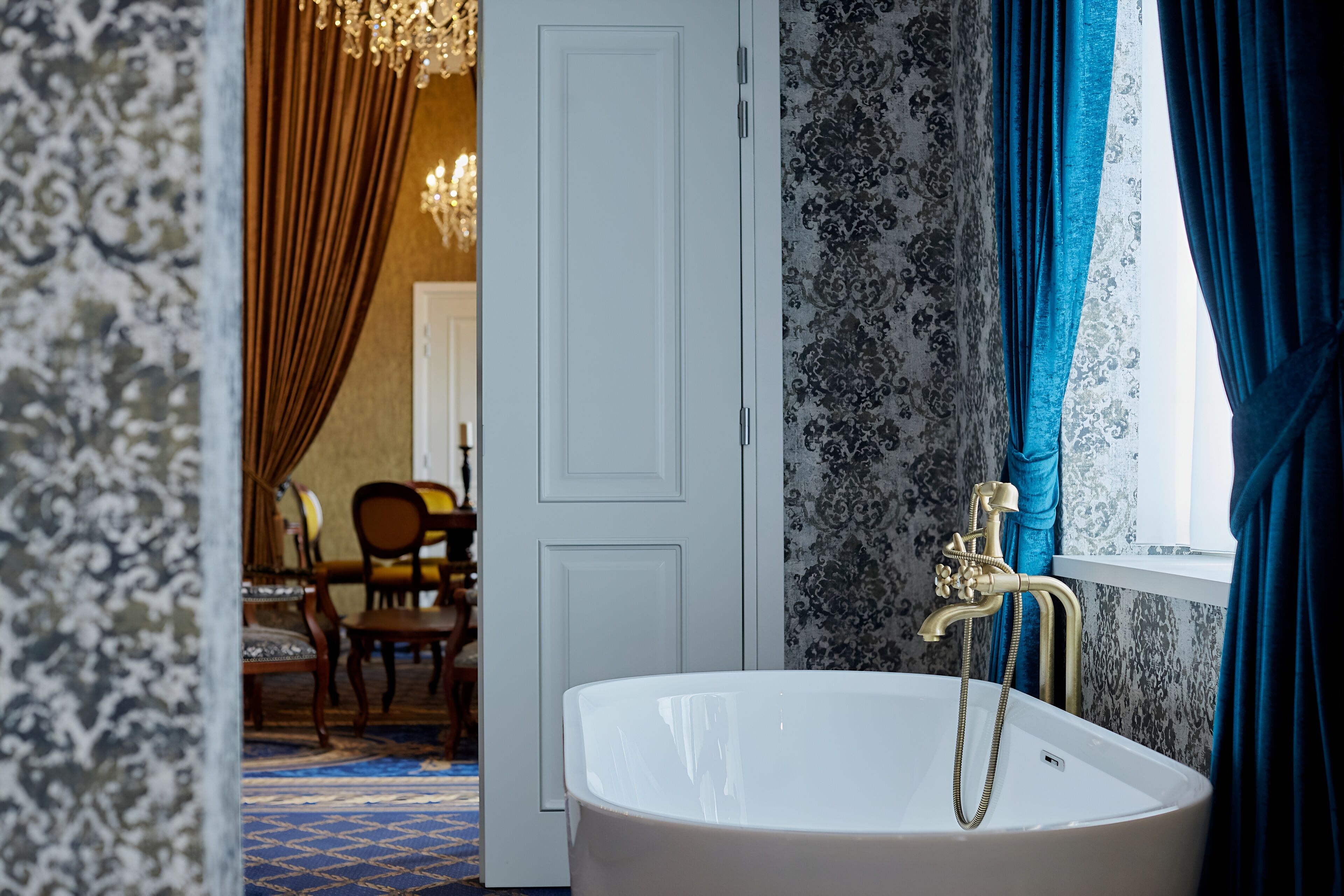 Une salle de bain avec une baignoire blanche, un robinet doré et une fenêtre ornée de rideaux bleus.