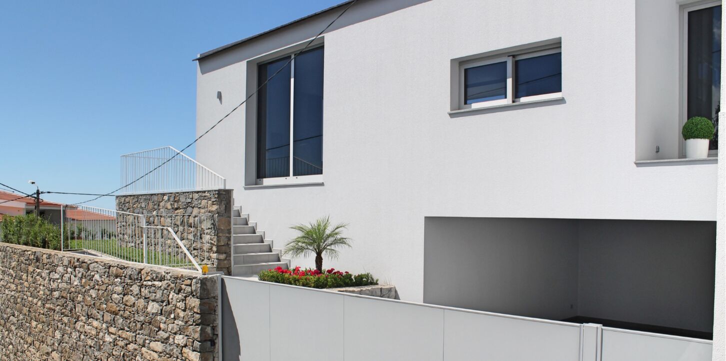 Un bâtiment moderne avec un escalier en pierre, un petit jardin agrémenté de fleurs rouges et un ciel dégagé.