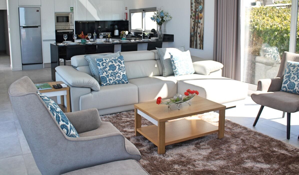 A modern living room with a sofa, coffee table, and a view of a kitchen and dining area.