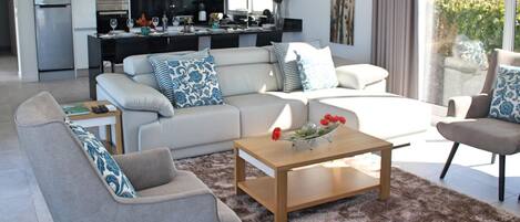 A modern living room with a sofa, coffee table, and a view of a kitchen and dining area.