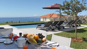 A poolside breakfast setup with lounge chairs, a table with breakfast items, and a view of the ocean. - Calheta Heights by Our Madeira (Calheta)